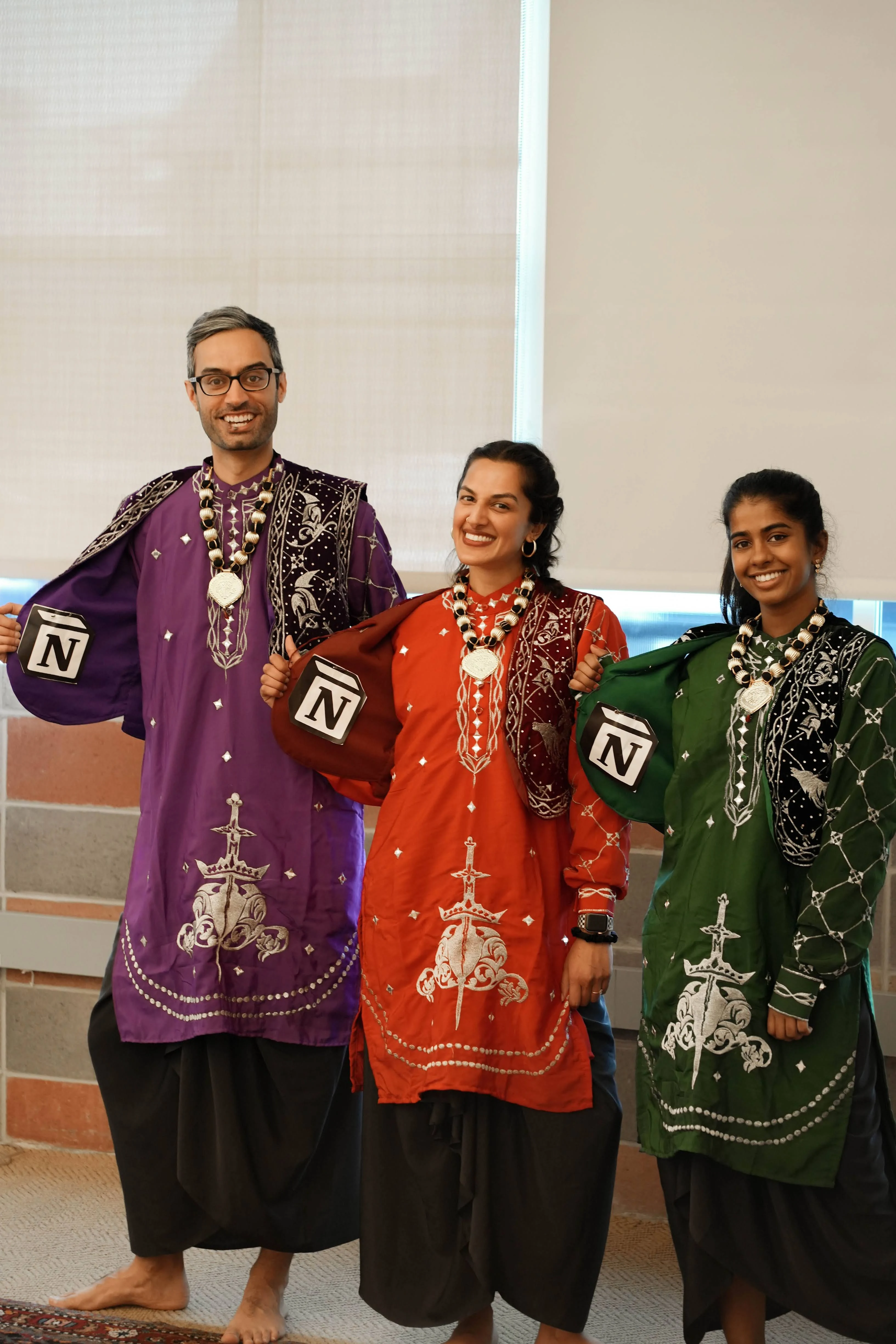 Saatchi and two colleagues in embroidered Punjabi dress and gold jewellery, holding Notion logo props before a Diwali performance